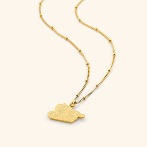 A close-up of the "With Hardship Comes Ease" Map Necklace in 18K gold plating. The pendant features a map outline of Palestine, engraved with the Arabic inscription "فَإِنَّ مَعَ الْعُسْرِ يُسْرًا" ("Verily, with hardship comes ease"), suspended from a delicate gold chain.