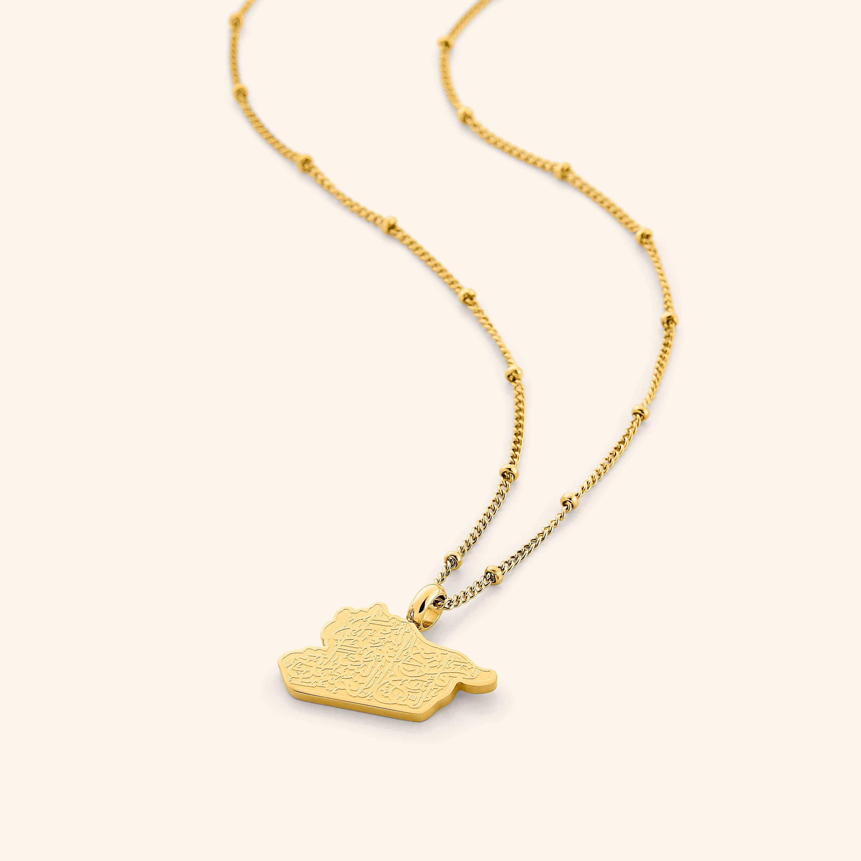 A close-up of the "With Hardship Comes Ease" Map Necklace in 18K gold plating. The pendant features a map outline of Palestine, engraved with the Arabic inscription "فَإِنَّ مَعَ الْعُسْرِ يُسْرًا" ("Verily, with hardship comes ease"), suspended from a delicate gold chain.