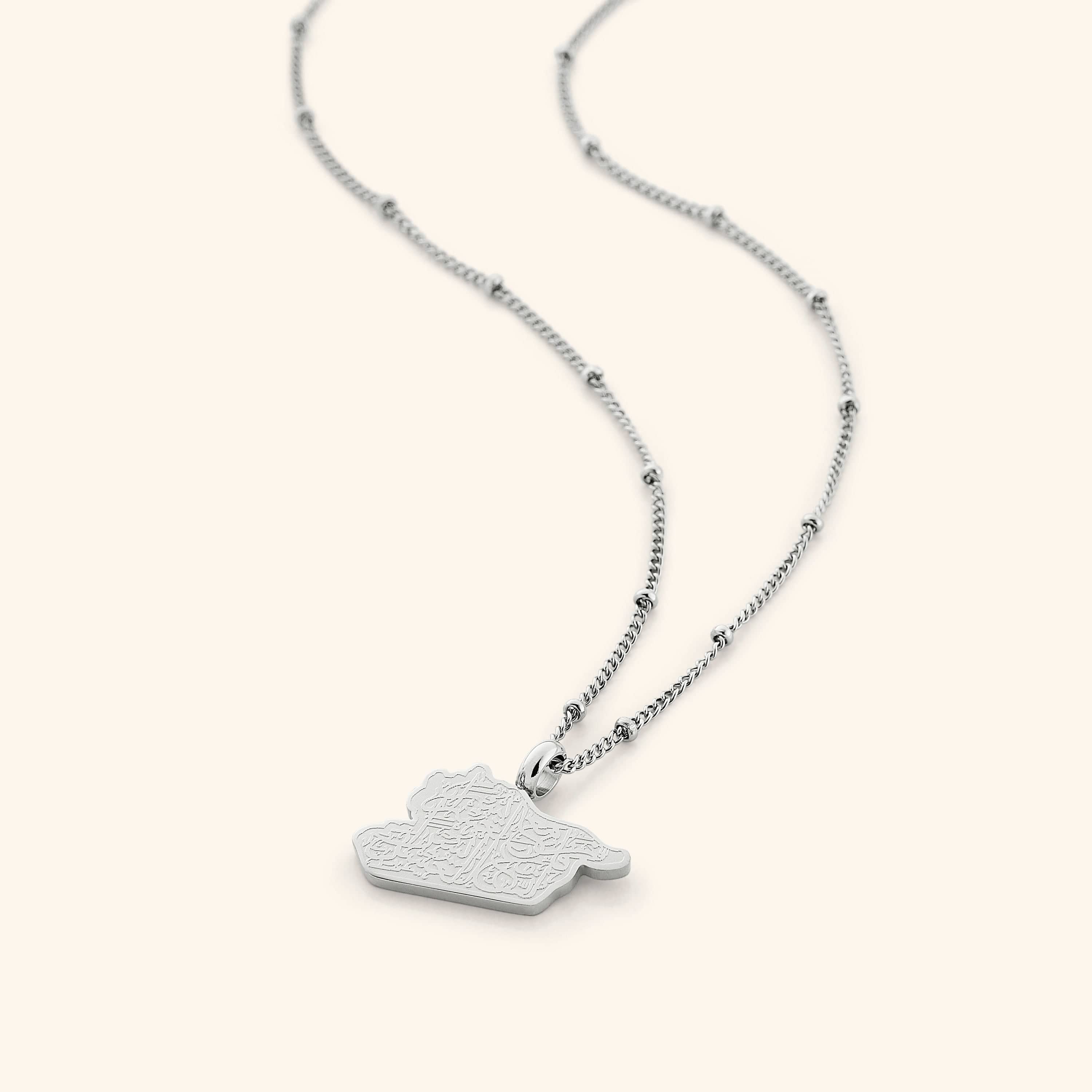 The "With Hardship Comes Ease" Map Necklace in a polished silver finish, showcasing a map outline of Palestine with the engraved Arabic inscription "فَإِنَّ مَعَ الْعُسْرِ يُسْرًا" ("Verily, with hardship comes ease"), hanging from a slender silver chain.