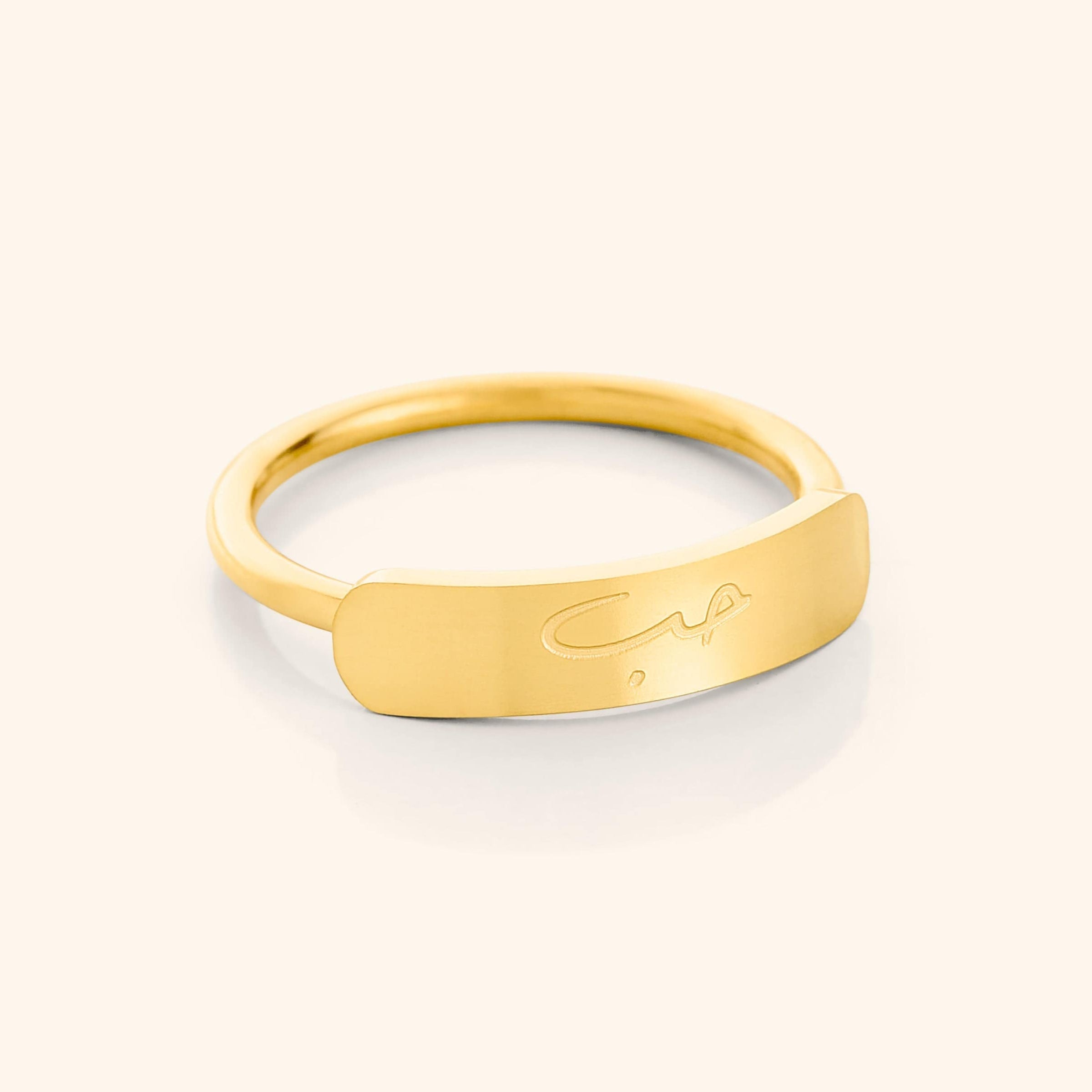 Close-up of a slim gold ring with a rectangular bar centerpiece engraved with the Arabic word meaning "love," shown on a plain background.