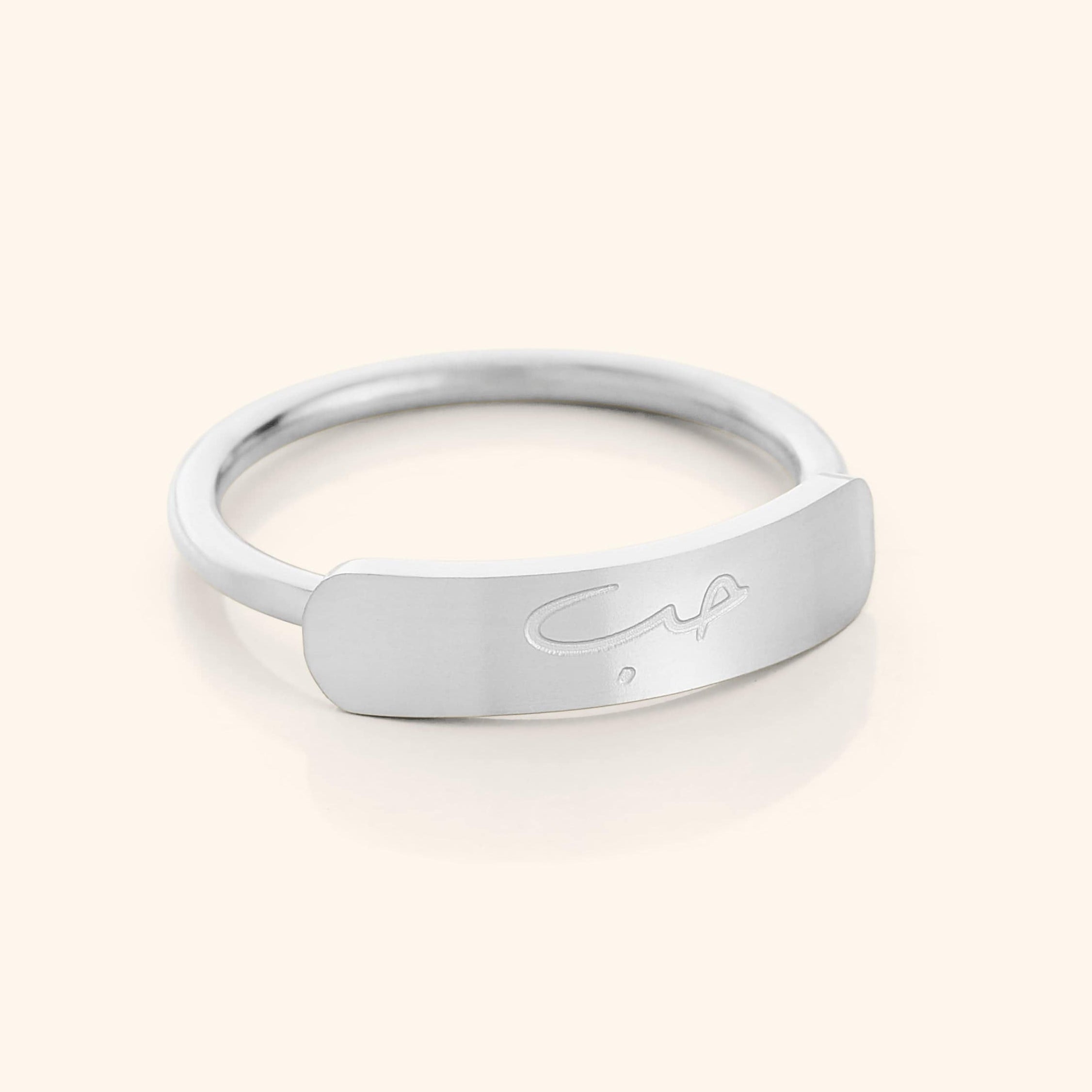 Close-up of a slim silver ring with a rectangular bar centerpiece engraved with the Arabic word meaning "love," shown on a plain background.