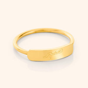 Close-up of a slim gold ring with a rectangular bar centerpiece engraved with the Arabic word meaning "patience," shown on a plain background.