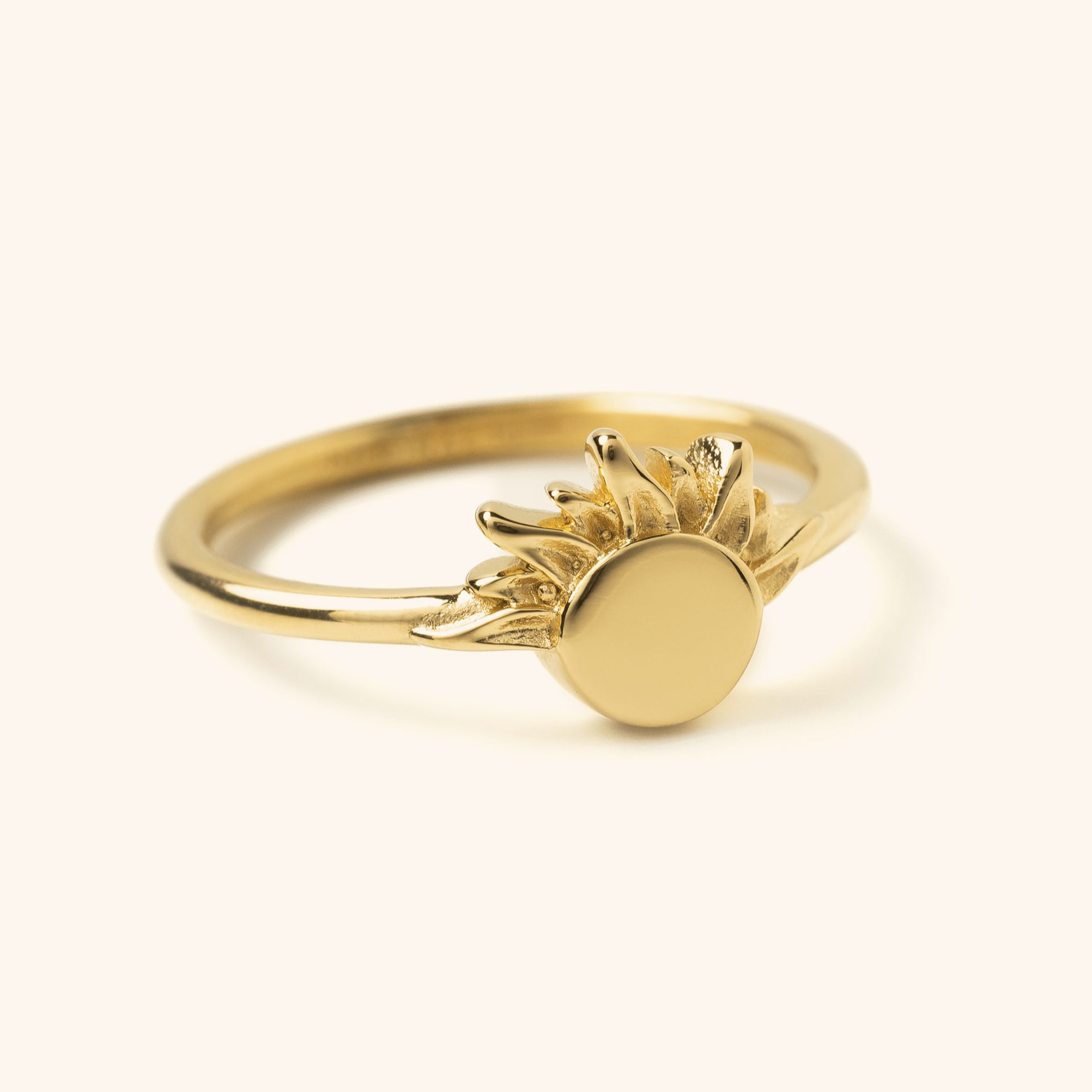 Gold ring featuring a circular sun design with textured rays extending outward, photographed against a neutral background.