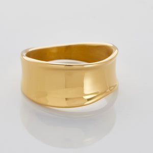 Close-up of a wide, wavy gold band ring with a smooth, melted-like design, photographed against a neutral background.
