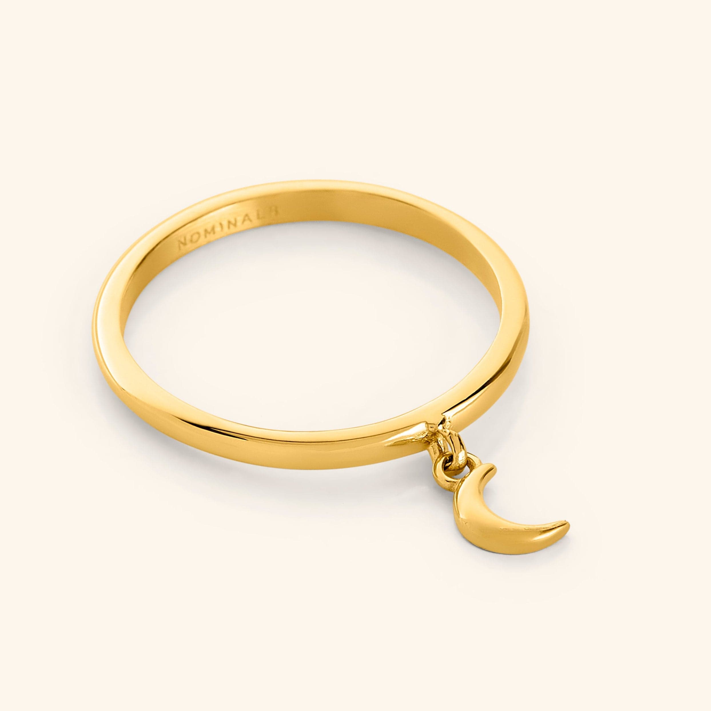 Close-up of a gold ring with a small dangling crescent moon charm attached to the band.