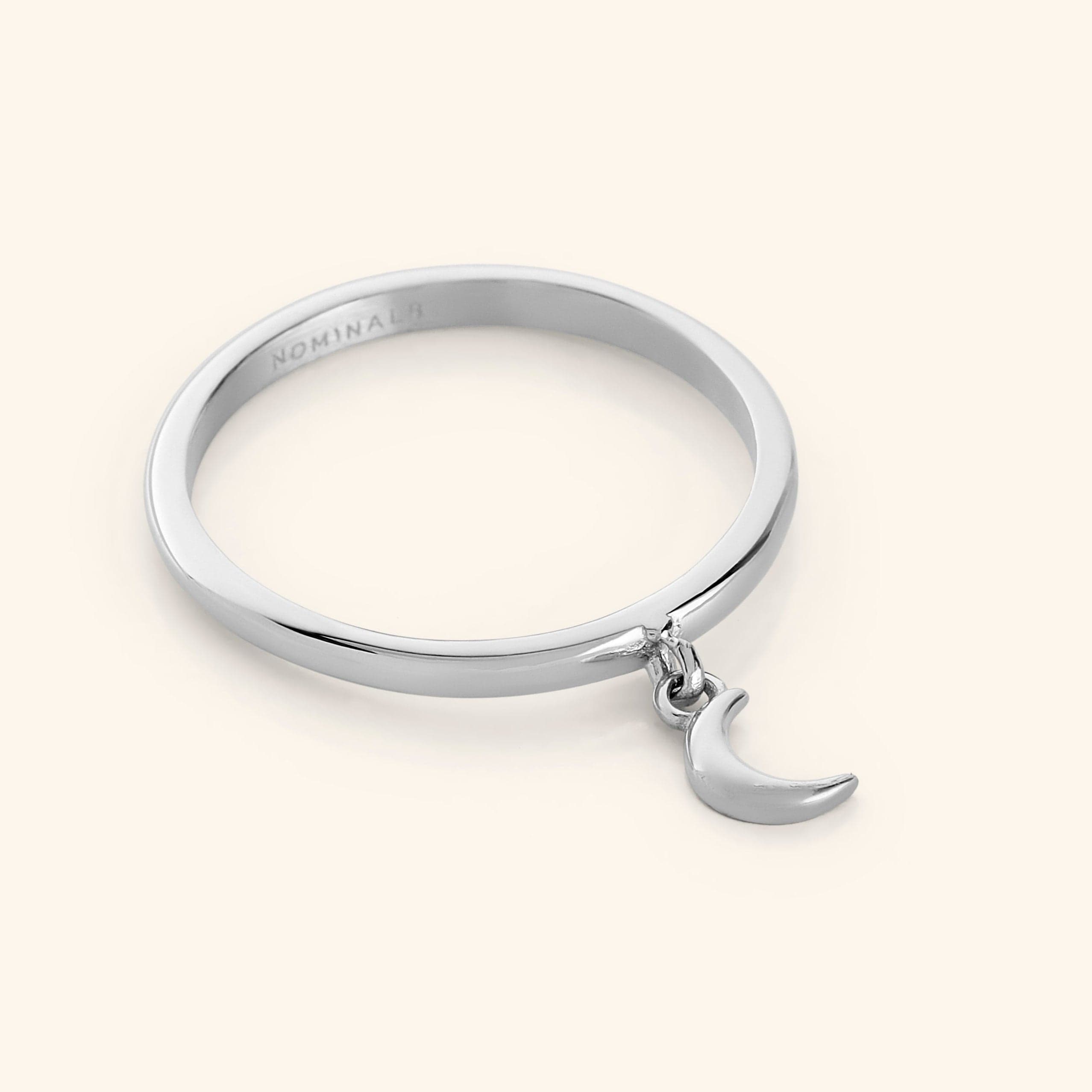 Close-up of a silver ring with a small dangling crescent moon charm attached to the band.