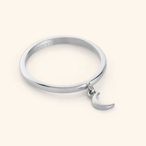 Close-up of a silver ring with a small dangling crescent moon charm attached to the band.