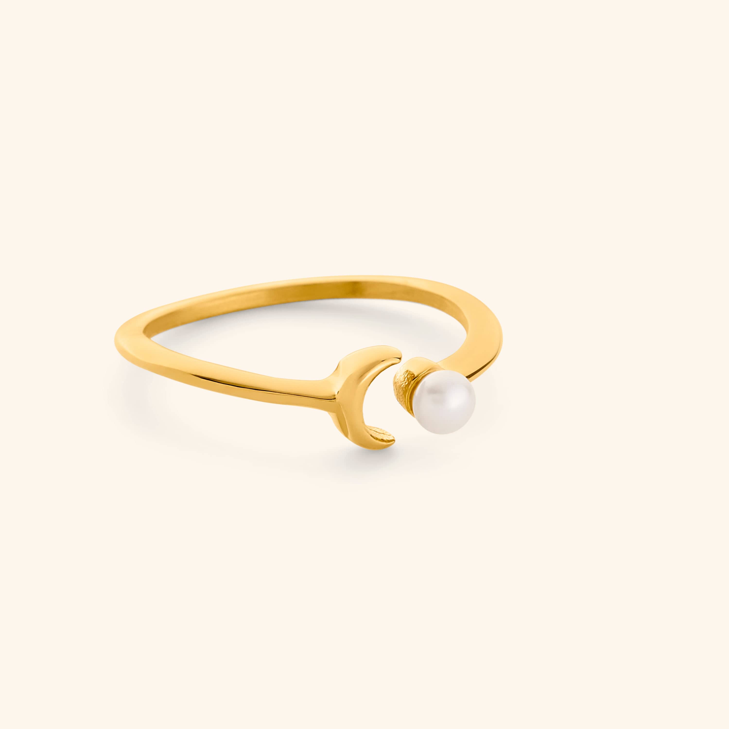Gold ring with a pearl and moon design on a light background.