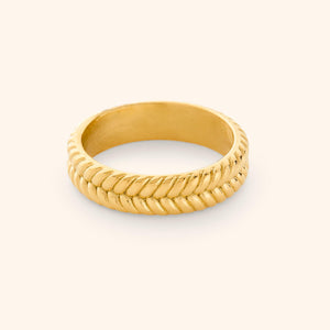 Close-up of a gold herringbone ring with a textured braided design wrapping around the entire band, photographed against a neutral background.