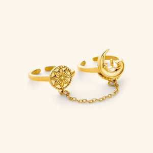 A set of two 18K gold plated rings connected by a thin chain: one ring is carved with a crescent and رحلة (journey) in Arabic, the other stamped with a floral coin.