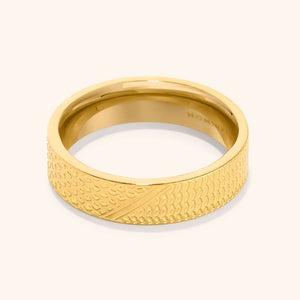 A close-up of the Keffiyeh Ring in 18K gold plating, featuring intricate engravings inspired by the traditional Palestinian keffiyeh pattern, including fishnet designs, bold lines, and olive leaves.