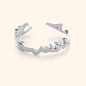 Close-up of a silver ring shaped into Arabic calligraphy spelling "Love Yourself First," on a neutral background.