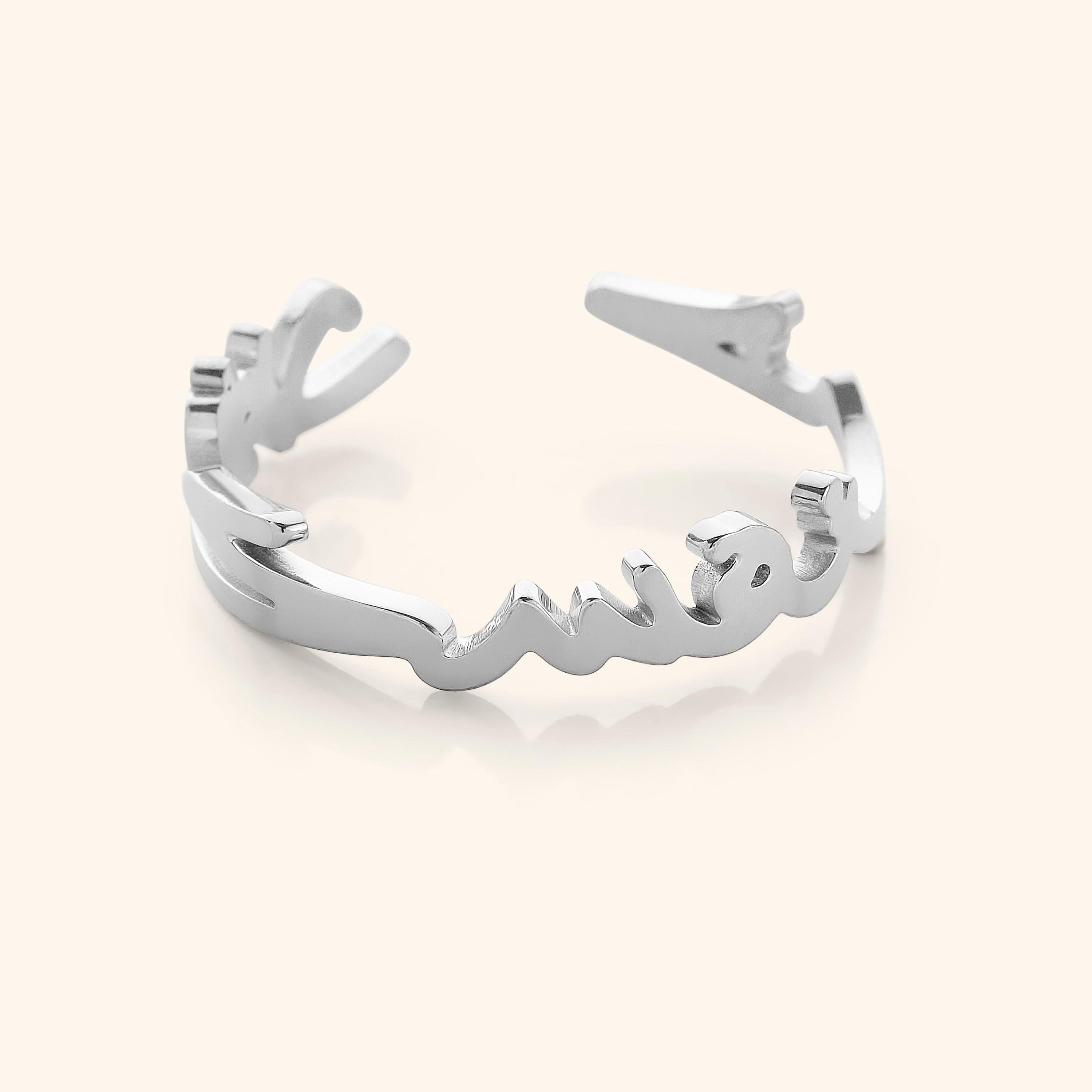 Close-up of a silver ring shaped into Arabic calligraphy spelling "Love Yourself First," on a neutral background.