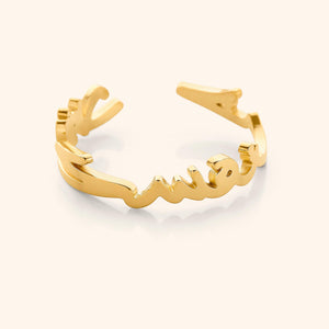 Close-up of a gold ring shaped into Arabic calligraphy spelling "Love Yourself First," on a neutral background.