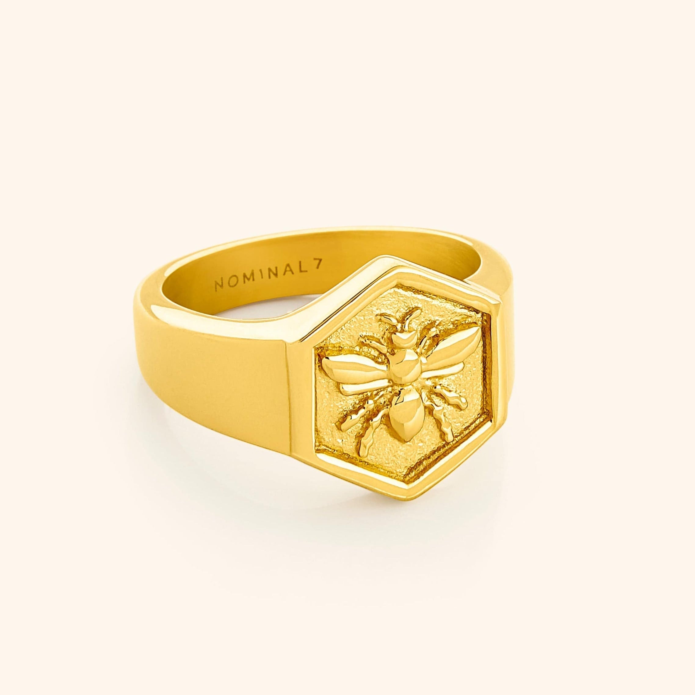 Gold hexagon-shaped ring with a raised bee design on the face, engraved with the word “NOMINAL” inside the band.
