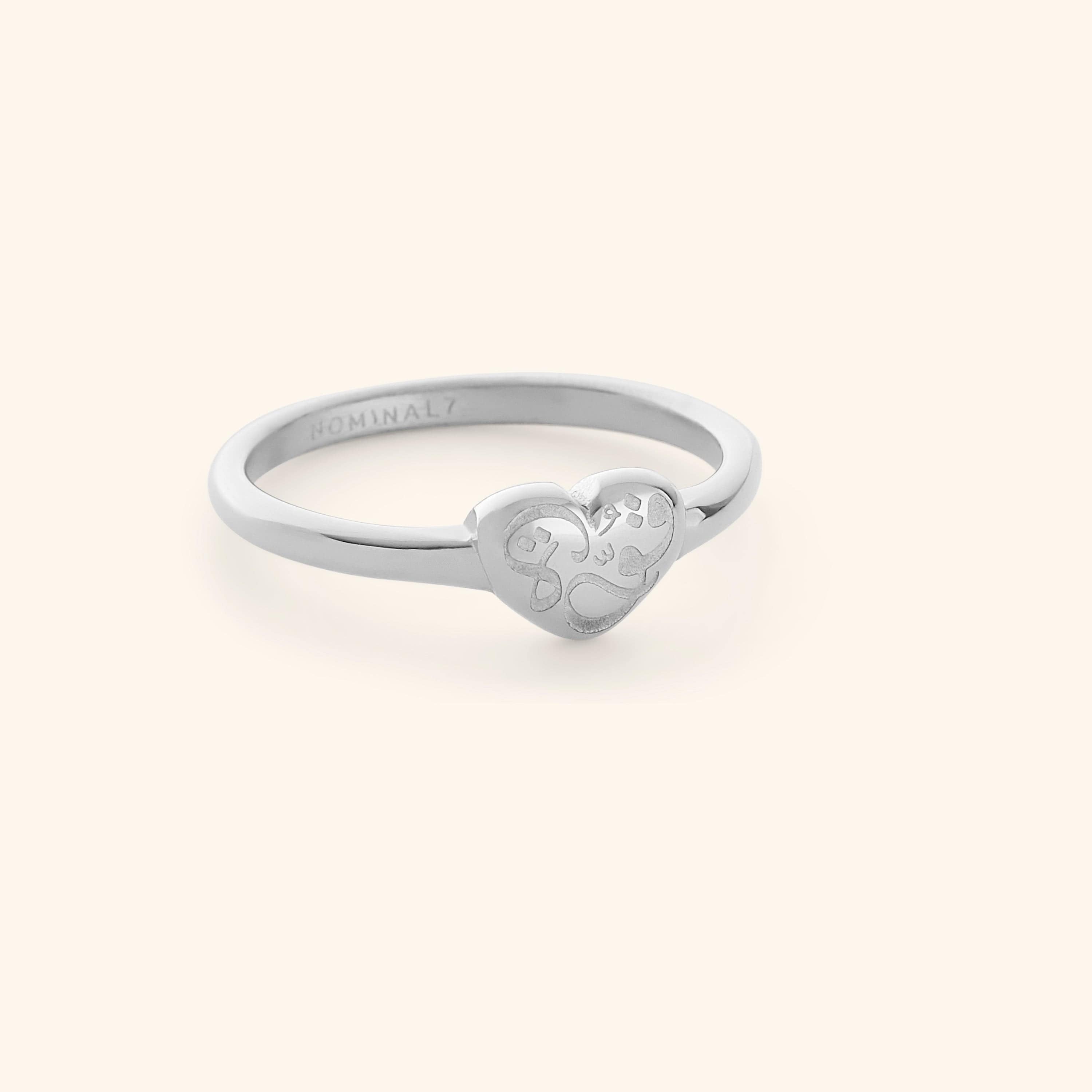 Silver ring with a heart-shaped design with calligraphy that reads "Quwa", shot on a white background