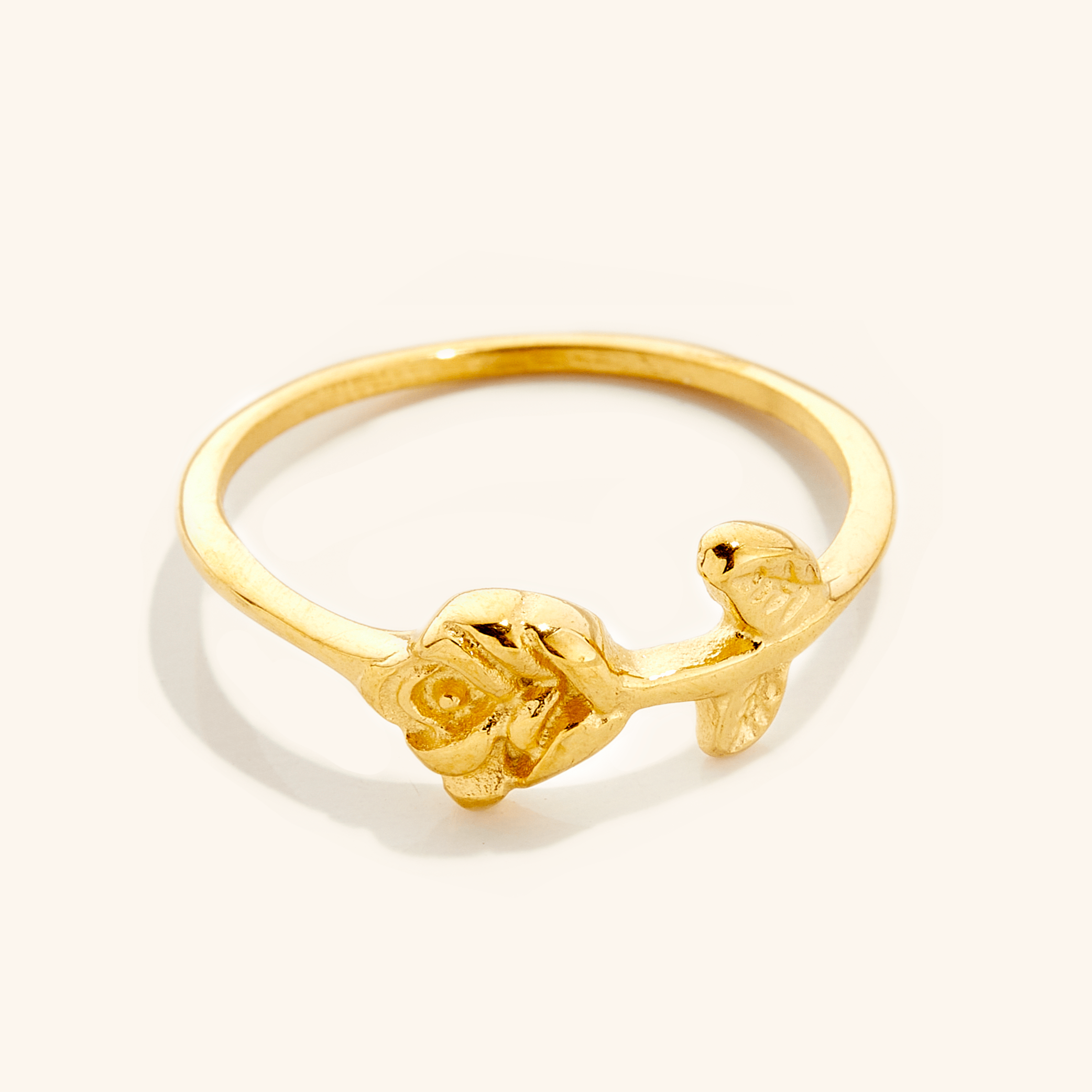 Gold ring featuring a delicate rose design with carved petals and leaves on a slim band, photographed against a neutral background.