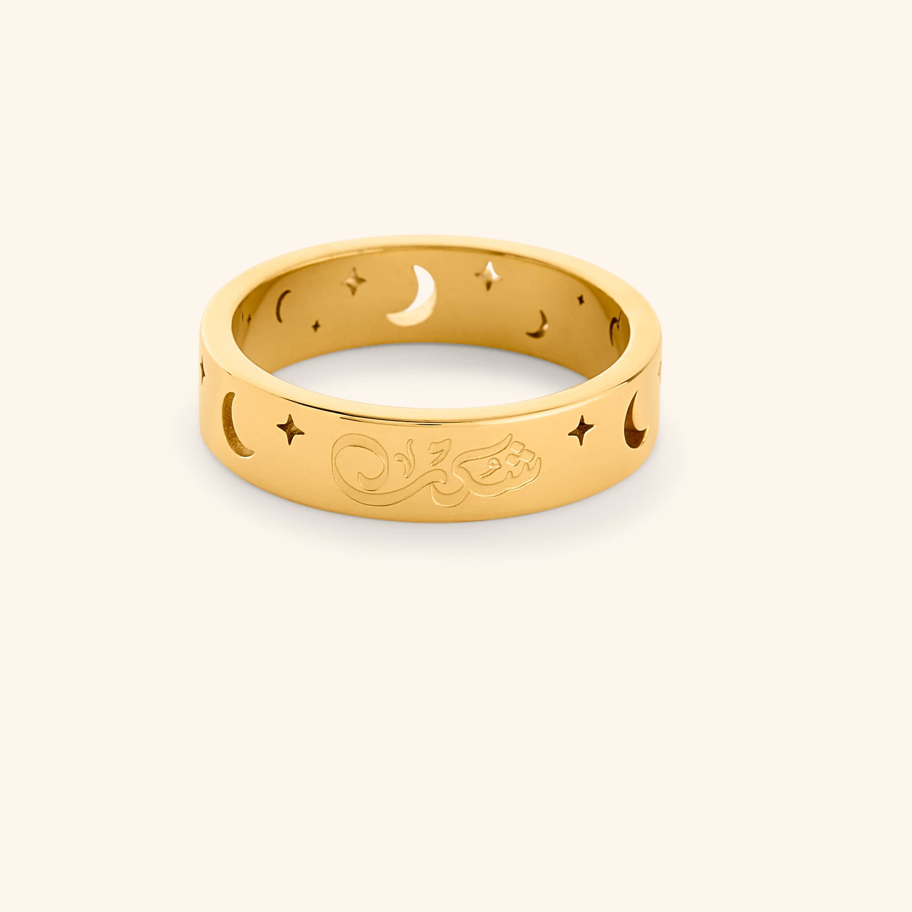 Gold ring with cutout star and moon design and an engraving that reads "Shukr", shot on a white background