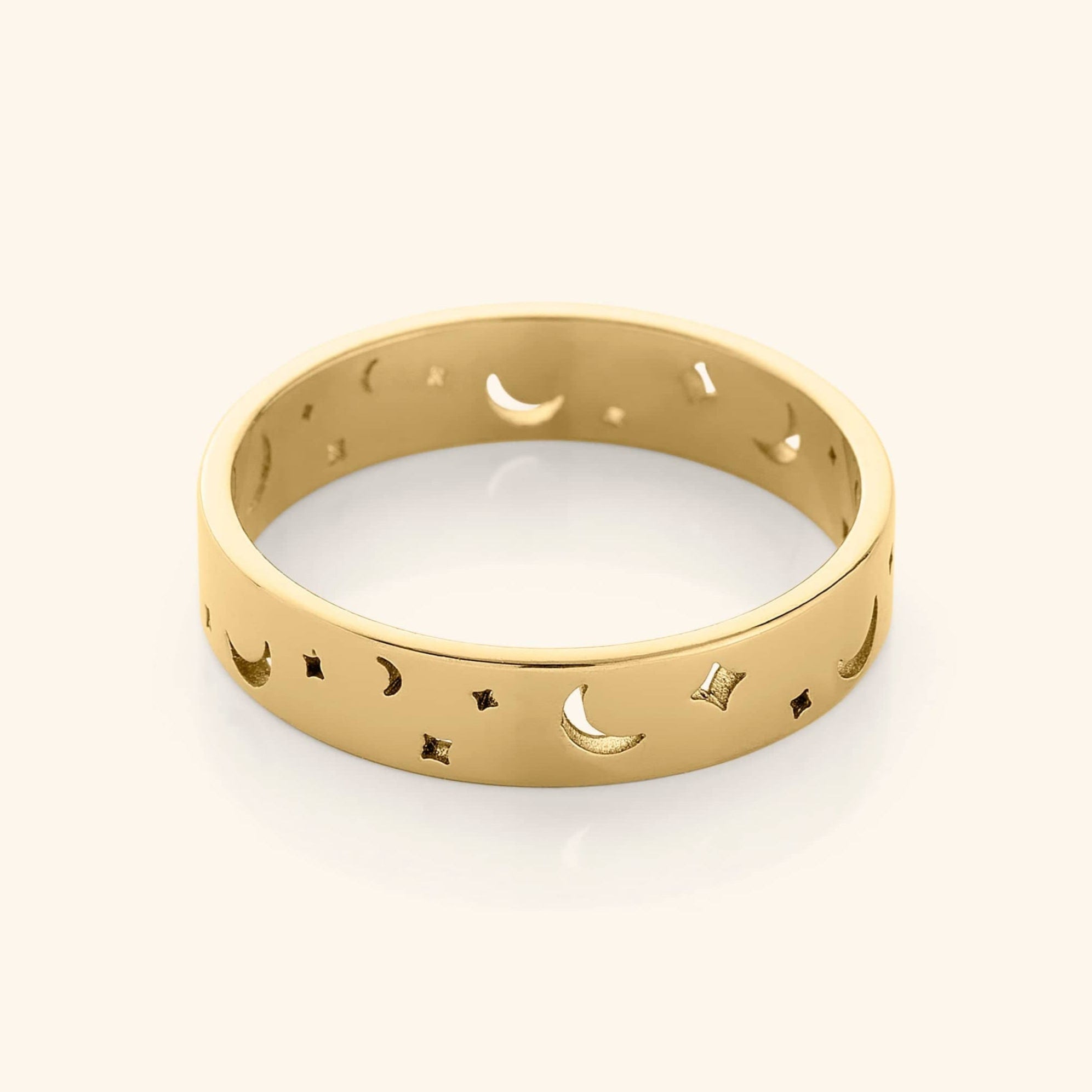 Gold band ring with cutout crescent moons and star shapes, displayed on a plain background.