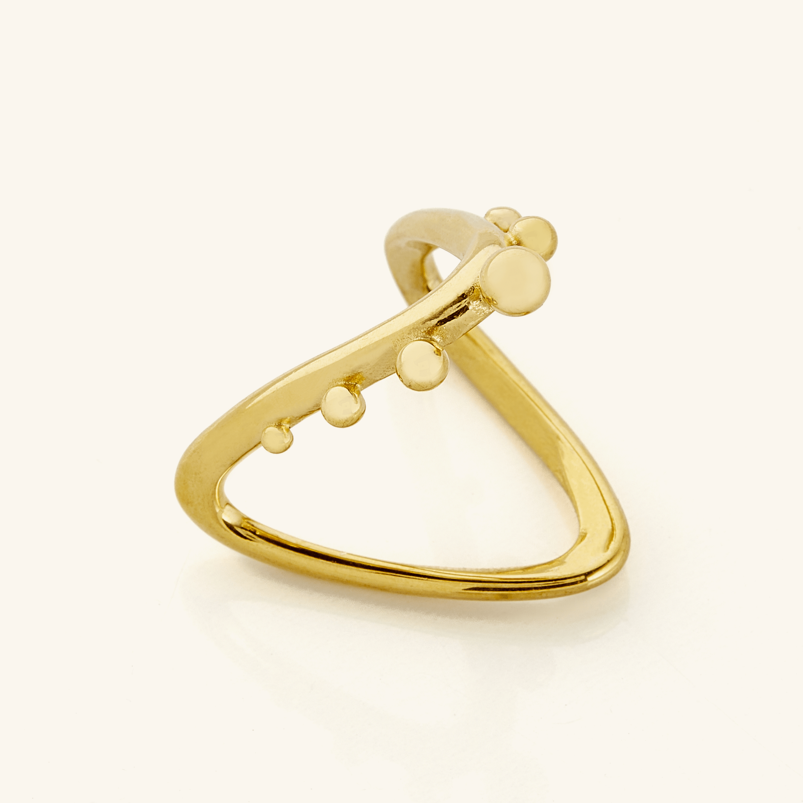 Close-up of a gold Orbiting Ring featuring a V-shaped band with raised circular accents along one side, photographed on a light background.