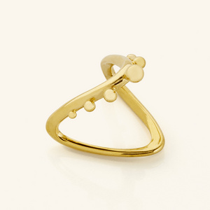 Close-up of a gold Orbiting Ring featuring a V-shaped band with raised circular accents along one side, photographed on a light background.