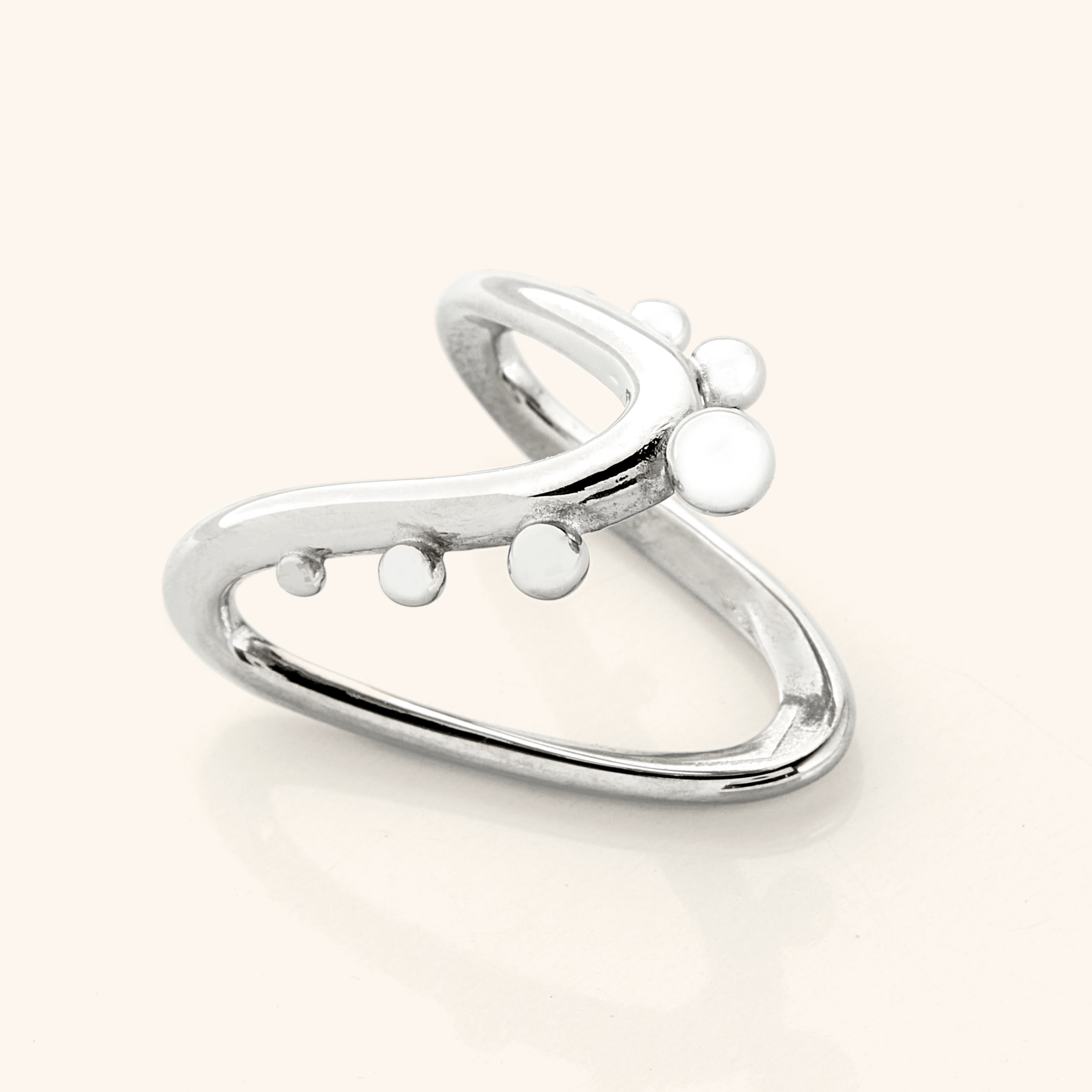 Close-up of a silver Orbiting Ring with the same V-shaped band and raised circular details, photographed on a light background.