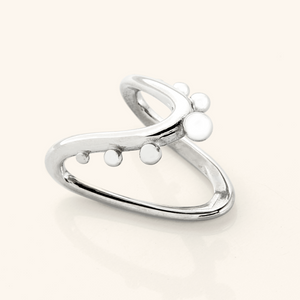 Close-up of a silver Orbiting Ring with the same V-shaped band and raised circular details, photographed on a light background.