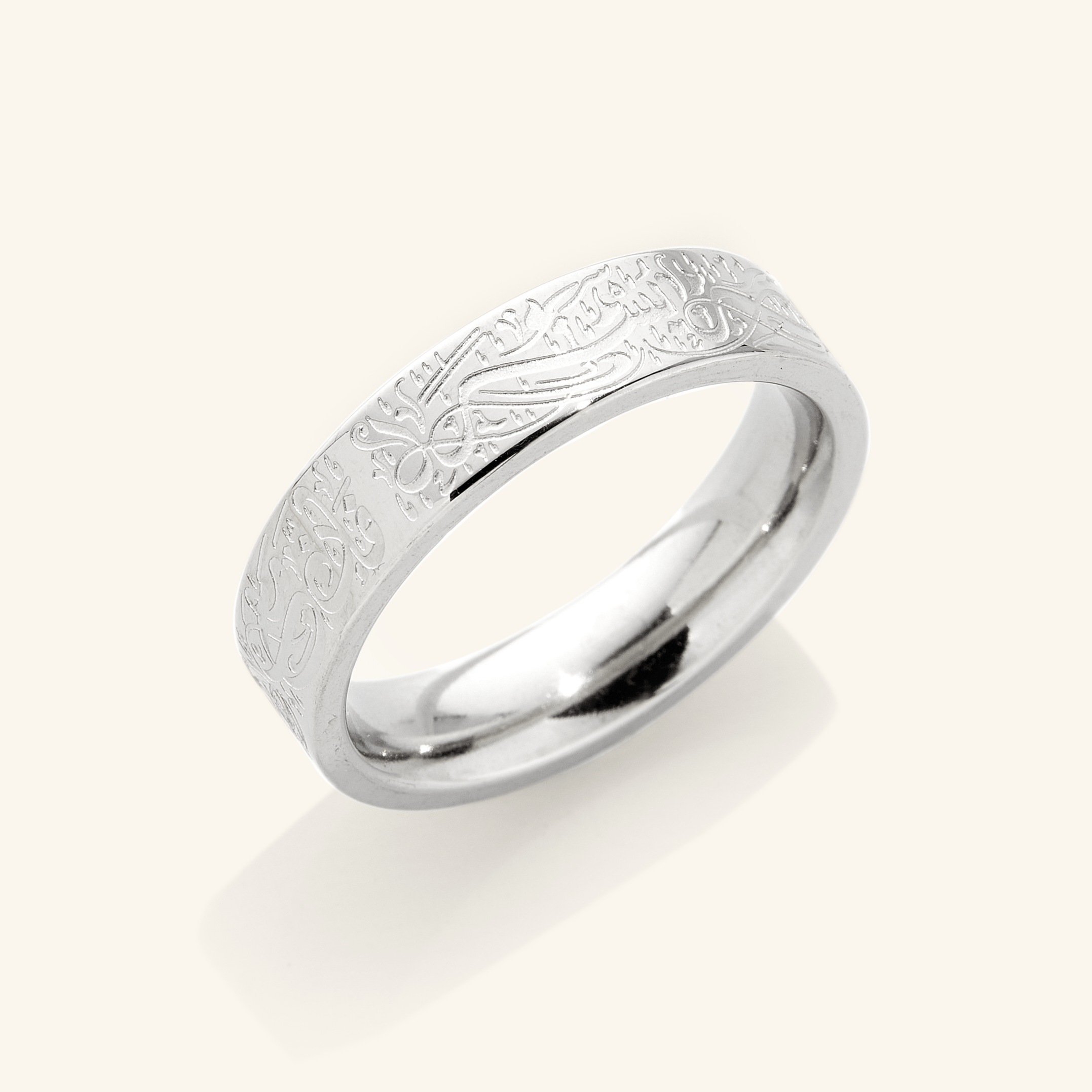 A silver ring with an intricate design etched around the outer surface. The design appears to be Arabic script meaning "With Hardship Comes Ease". The ring is displayed on a bright background with a soft shadow underneath. 