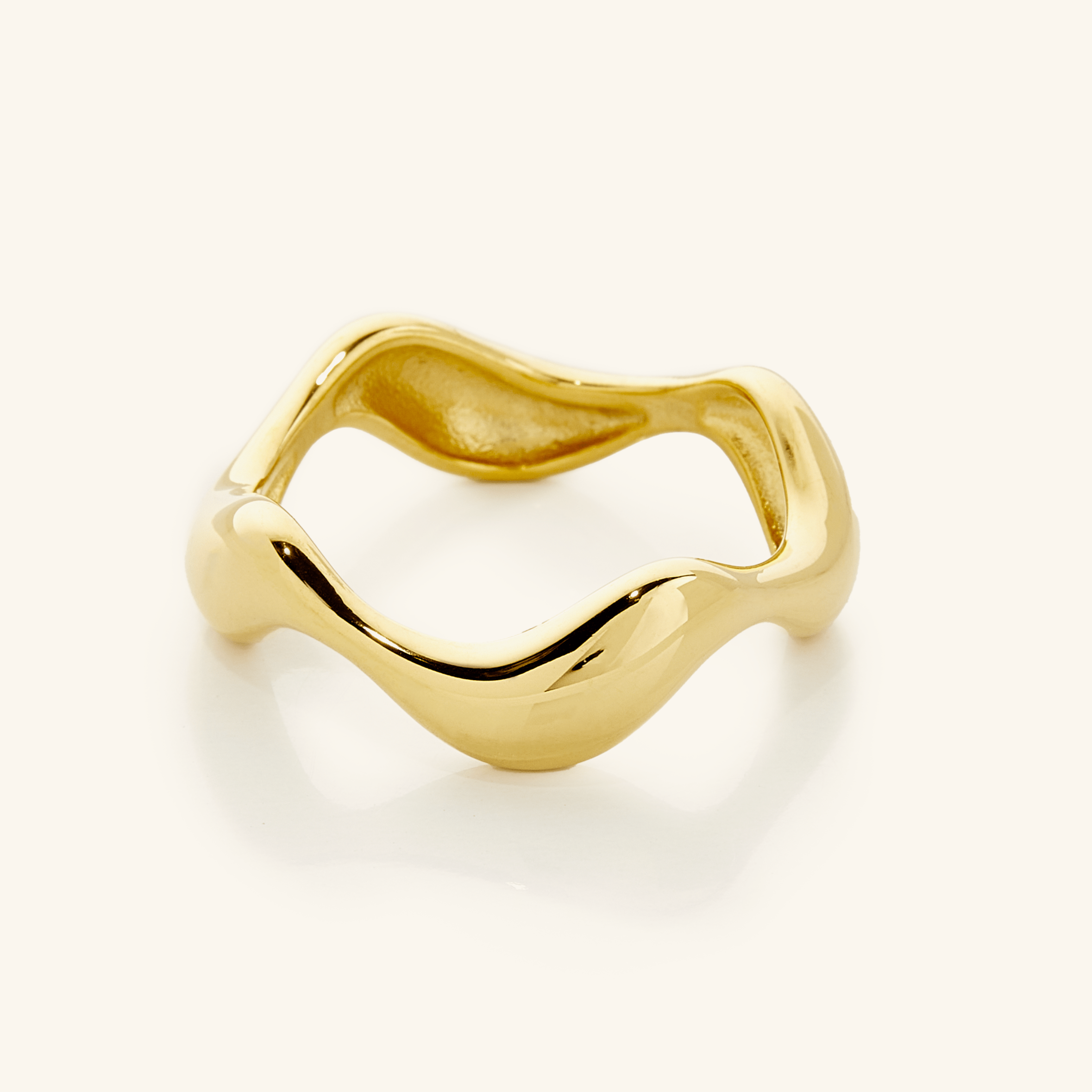 Close-up of a polished gold ring with a fluid, wavy band design, photographed against a neutral background.