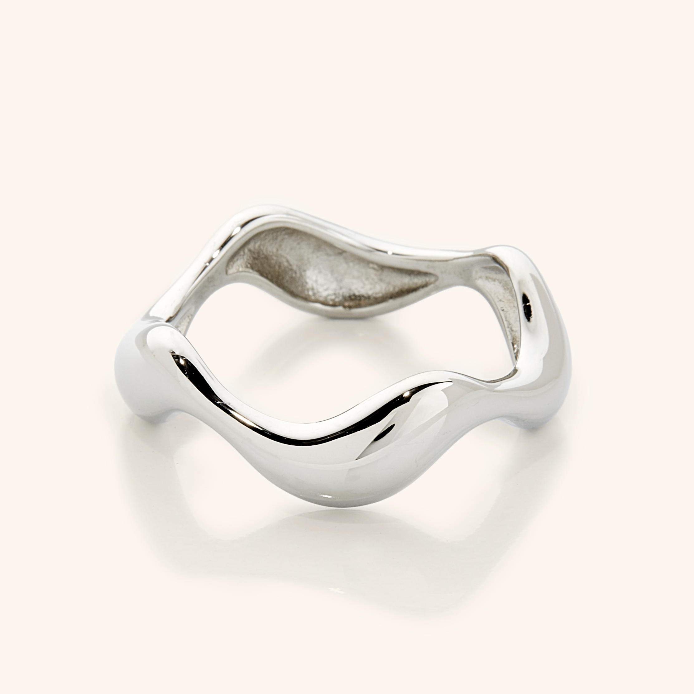 Close-up of a polished silver ring with a sculpted wavy band, photographed against a neutral background.