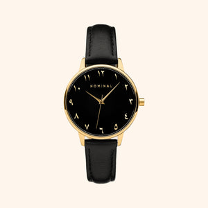 Black mesh strap watch with minimalist Arabic numerals and gold details, displayed against a neutral background